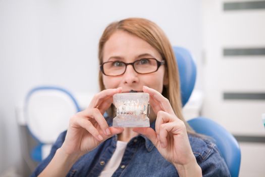 Female patient holding dental model with braces, waiting for medical exam at the dentist