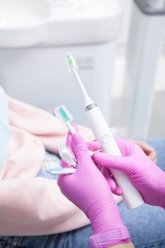 Vertical close up of a dentist holding electric toothbrush and three different replacement heads