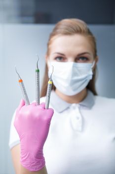 Vertical portrait of a young female dentist in medical face mask holding up dental tools like claws in her hand