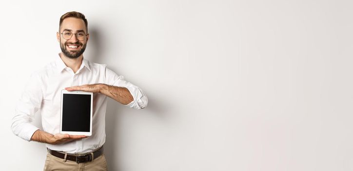 Smiling manager showing something on digital tablet screen, demonstrating website, standing over white background.