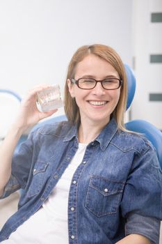 Vertical shot of a mature woman laughing at dental clinic, holding dental model with braces