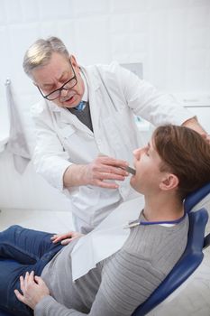 Vertical shot of an elderly dentist working at his clinic, checking teeth of patient