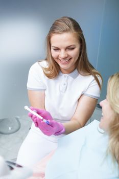 Vertical shot of a young female dentist showing teeth whitening gel to female patient