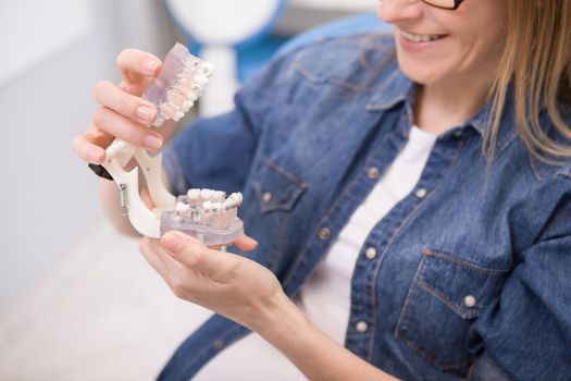 Cropped shot of a woman smiling, looking at jaw model with braces