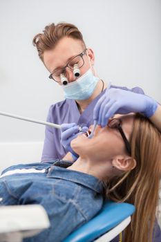 Vertical shot of a dentist wearing microscope glasses, treating teeth of patient
