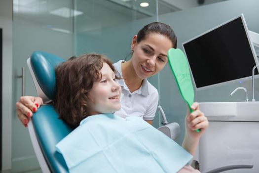 Adorable young boy checking teeth in the mirror after dental procedure at dentists office