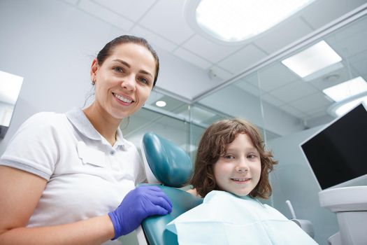 Beautiful female dentist and her young patient smiling to the camera after dental checkup