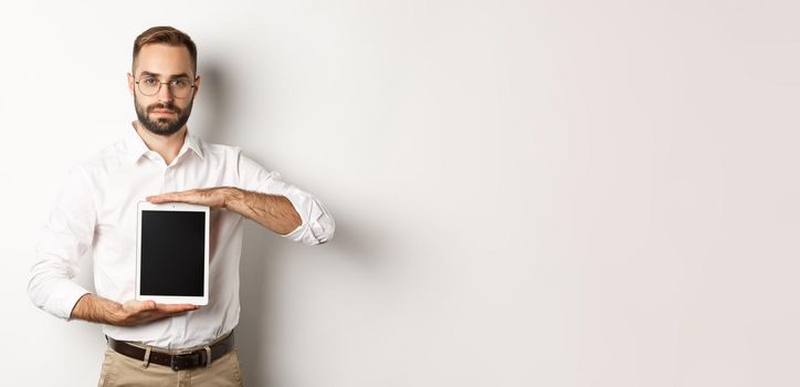 Confident bearded man showing digital tablet screen, demonstrating app, standing over white background.