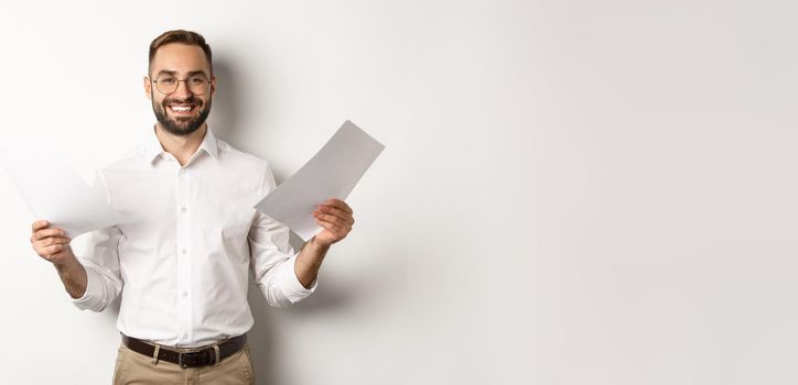 Satisfied boss smiling while holding good report, reading documents, standing over white background.