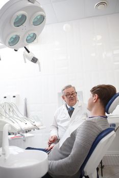Vertical shot of a senior male dentist having appointment with patient at the clinic