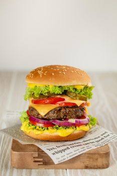 Delicious burger with meat, melted cheese, dripping sauce and vegetables on white rustic background. Freshly made tasty hamburger, close-up.