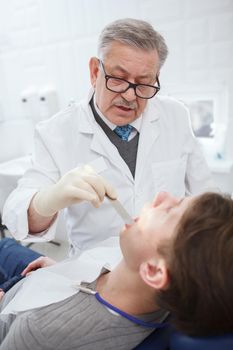 Vertical shot of a professional dentist talking to the patient while examining his teeth