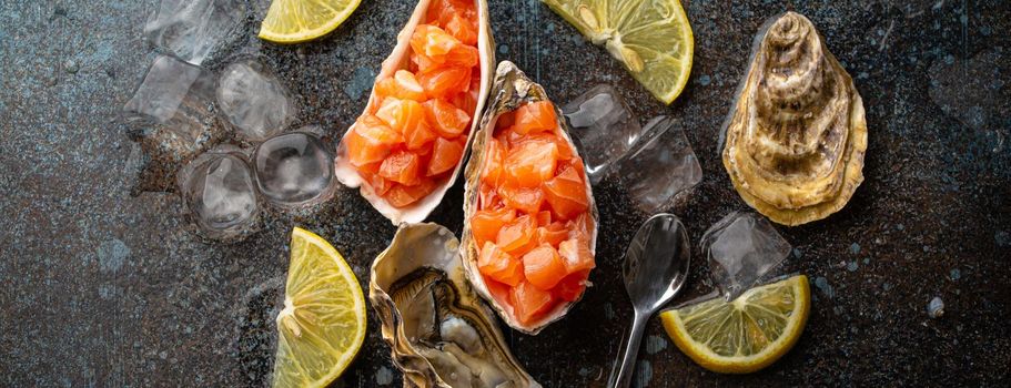 Delicious salmon tartare raw chopped in cubes served in oyster shells with lemon wedges and ice on blue stone rustic background, seafood appetizer or starter top view