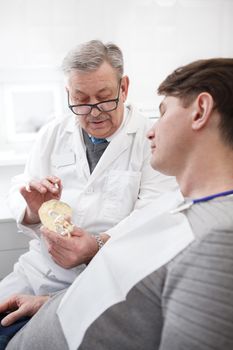 Vertical shot of a senior male dental surgeon talking to his patient