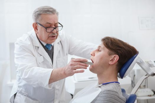 Experienced senior dentist examining teeth of a patient