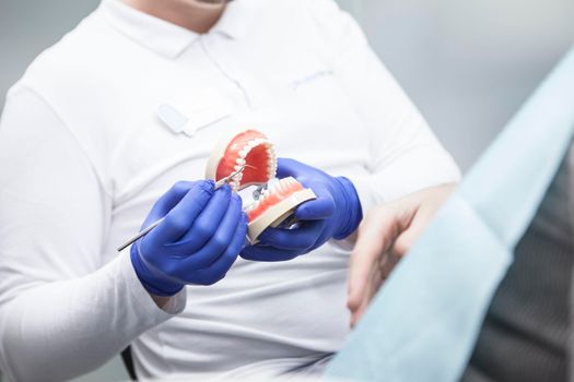 Unrecognizable dentist showing dental treatment on dentures model