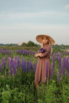 A beautiful woman in a straw hat walks in a field with purple flowers. A walk in nature in the lupin field.