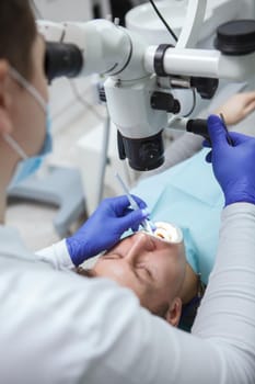 Vertical cropped shot of a male patient having dental treatment by experienced dentist, using microscope