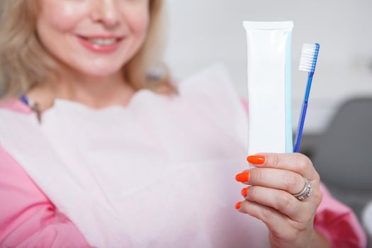 Cropped close up of tootbrush and toothpaste smiling woman is holding