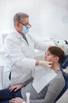 Vertical shot of a professional dentist wearing medical face mask, examining lymphatic nods of patient prior to dental treatment