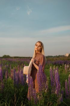 A beautiful woman in a straw hat walks in a field with purple flowers. A walk in nature in the lupin field.