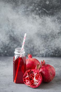 Freshly squeezed red pomegranate healthy juice in bottle with paper straw near whole and split in half fresh organic ripe pomegranate fruit with seed on grey concrete background .