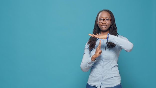 Female model doing timeout pause gesture on camera, showing t shape stop symbol with arms in studio. Refusing and rejecting problem to do pause sign and feel serious, signal no.