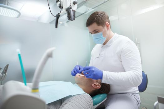Professional dentist working at his clinic, treating teeth of male patient