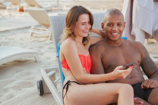 Happy handsome African man laughing, enjoying lying at the beach with his beautiful girlfriend, copy space. Young multiethnic couple enjoying travelling together to the seaside