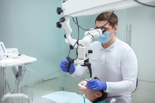 Professional dentist using dental microscope, treating teeth of patient