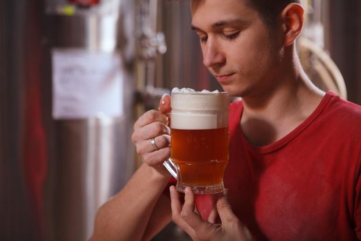Cropped shot of a male brewer smelling aromatic craft beer in a mug he is holding