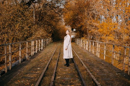 A beautiful long-haired woman walks through the autumn streets. Railway, autumn leaves, a woman in a light coat.