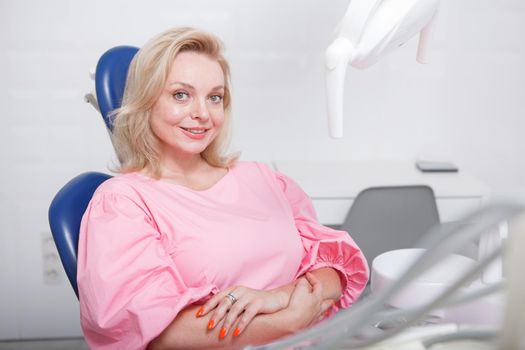 Cheerful mature woman sitting in a dental chair, smiling to the camera