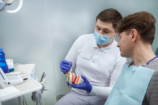 Male dentist educating his patient, explaining dental hygiene on a dental model, copy space