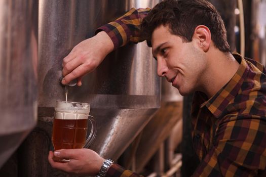 Handsome brewer smiling, pouring craft beer into a mug at his microbrewery