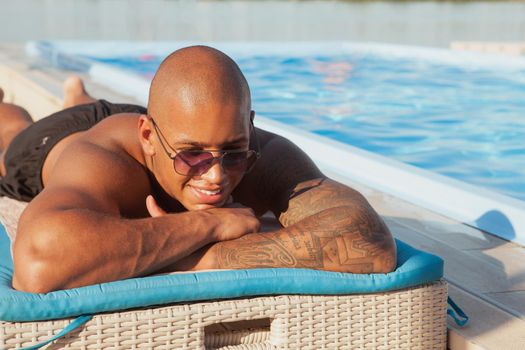 Happy African man smiling, enjoying sunbathing during his seaside vacation. Cheerful man lying near the swimming pool at the resort hotel