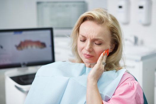 Mature woman having toothache, sitting in dental chair