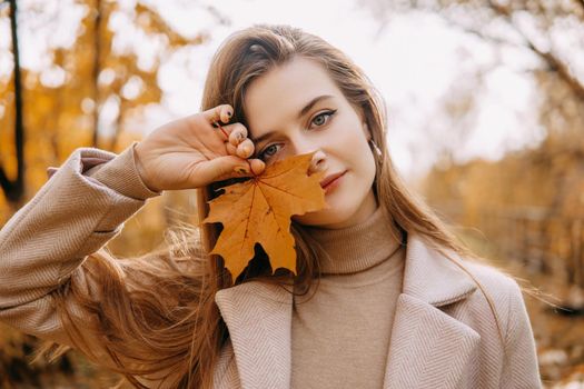 A beautiful long-haired woman walks through the autumn streets. Railway, autumn leaves, a woman in a light coat.