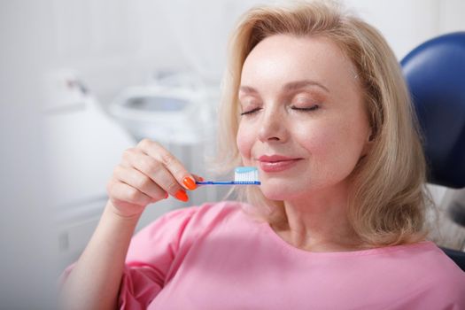 Mature woman smelling toothpaste on her toothbrush