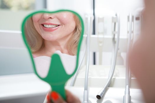 Close up of a mirror female patient is holding, looking at her teeth after dental treatment