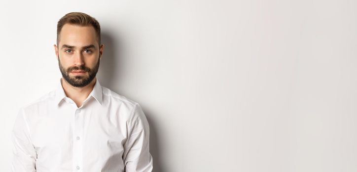 Close-up of serious businessman in white shirt looking at camera, standing confident.