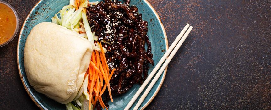 Chinese traditional dish sweet and sour deep fried glazed pork with vegetables and steamed bao bun on plate with on rustic concrete background top view, Asian meal with chopsticks copy space