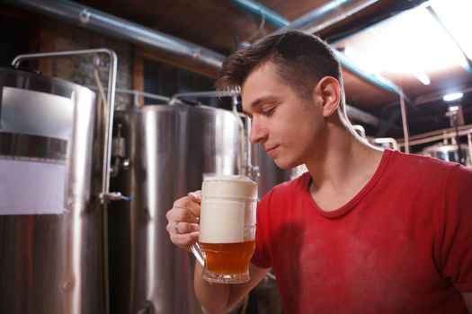 Handsome male brewer smelling freshly brewed beer in a glass, copy space