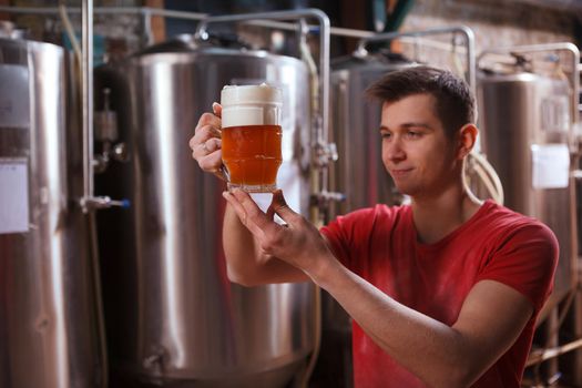 Selective focus on a beer mug in the hands of young professional brewer