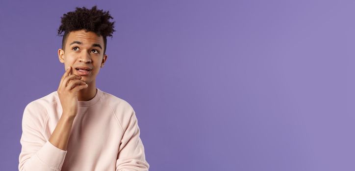 Waist-up portrait of thoughtful unsure young hispanic male student trying solve exercise, looking up thinking, pondering and calculating in mind, standing focused and indecisive purple background.