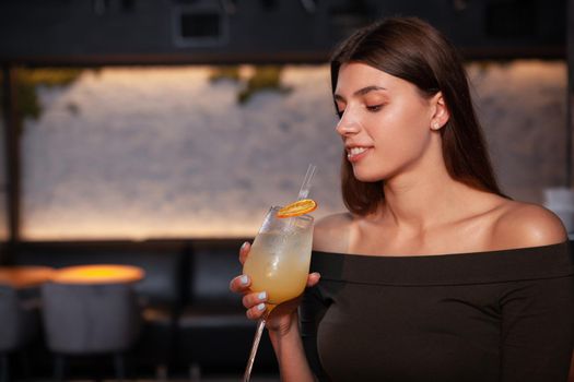 Close up of a gorgeous elegant woman having cocktail at the bar in the evening, copy space