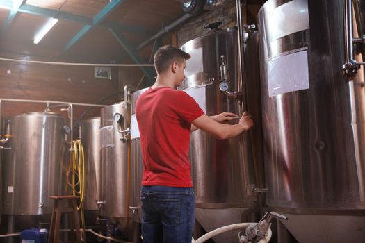 Rear view shot of a brewer working at microbrewery with metal beer tanks