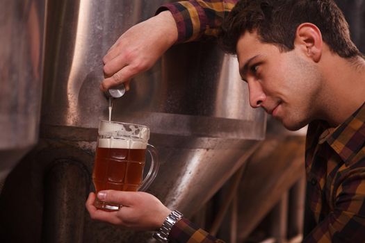 Cropped close up of a brewer pouring delicious fresh craft beer into a mug from beer tank at the brewery