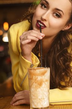 Delightful taste. Vertical portrait of a red lipped brunette sipping her cocktail seductively looking to the camera