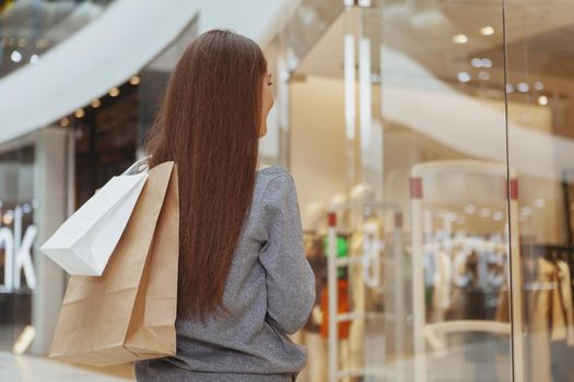 Rear view shot of a female customer at the shopping mall, holding paper bags with purchase. Woman walking at the mall, enjoying seasonal sales, copy space